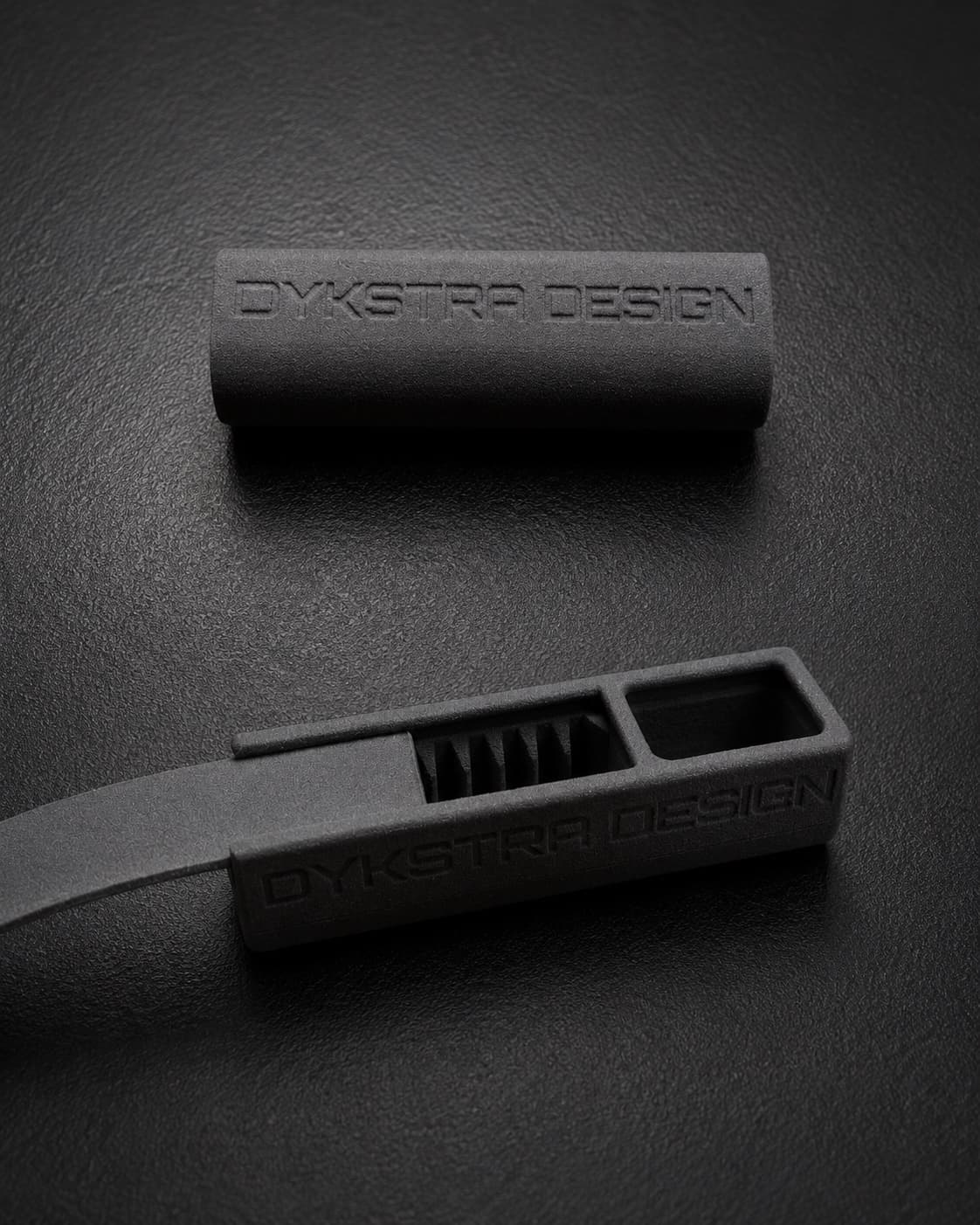 SLS-printed parts with an embossed Dykstra Design logotype: a grip sleeve and a ribbed clip housing